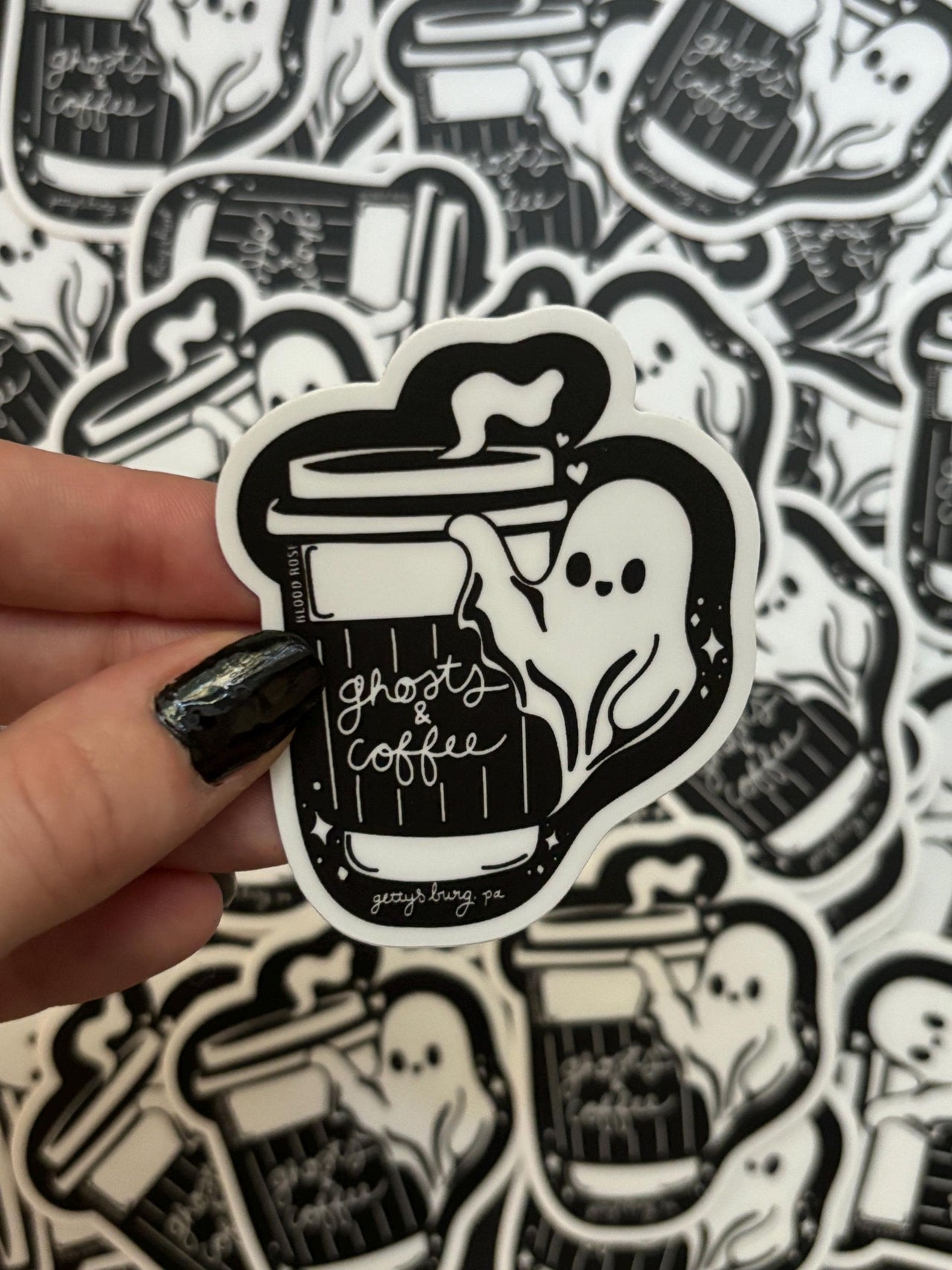 Sticker of a ghost holding a coffee cup with 'ghosts & coffee' text, held over a patterned background.